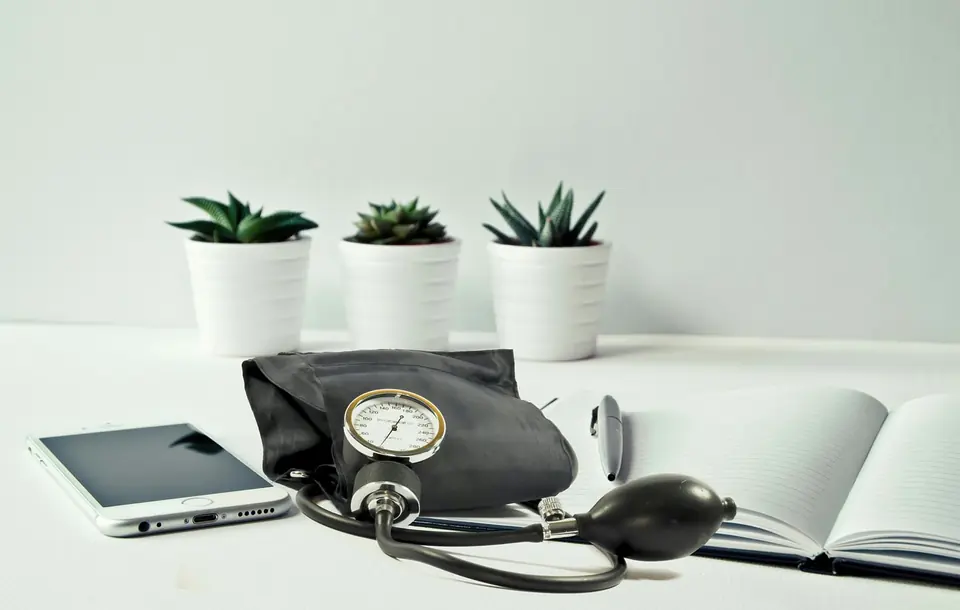 A home blood pressure monitor next to an open notebook for recording readings