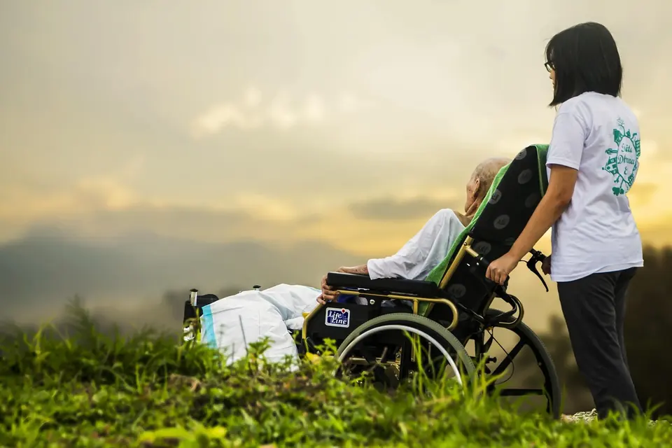 A carer pushing an older man in a wheelchair outdoors