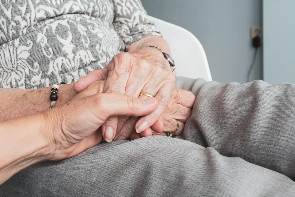 A younger person holding an older woman’s hands