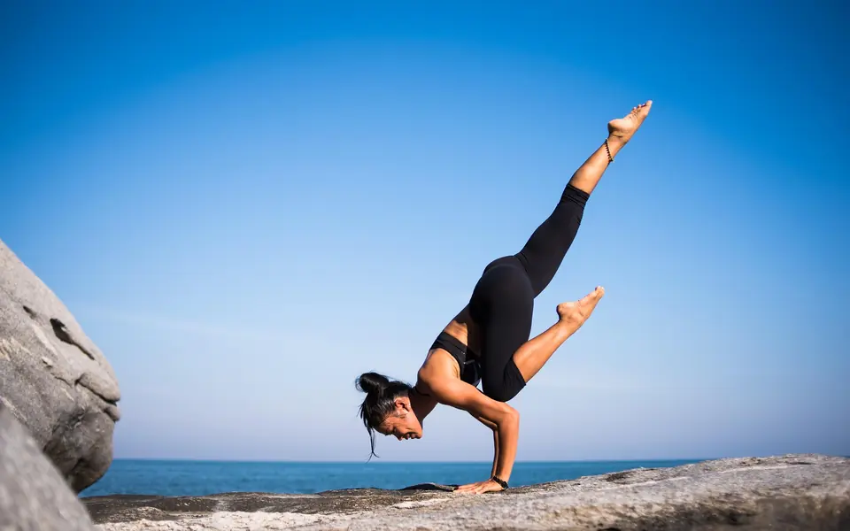 A woman holding a yoga balance pose on a rock by the sea